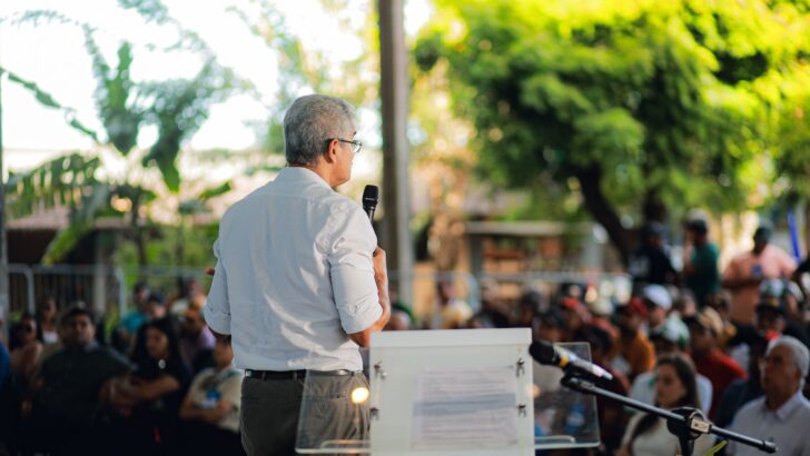 Professor de camisa clara fala ao microfone diante de participantes da palestra na Festa do Boi