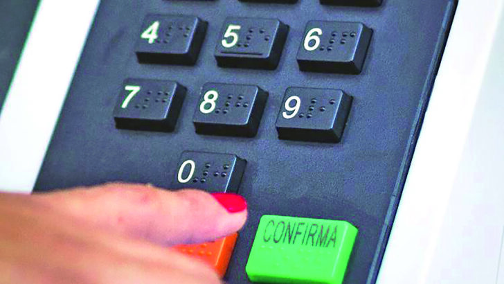 Mão de uma eleitora junto ao botão confirma da urna eletrônica