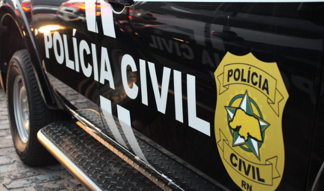 Imagem mostra a lateral de uma viatura preta da Polícia Civil do Rio Grande do Norte, com o nome da instituição em letras brancas e o brasão oficial em amarelo