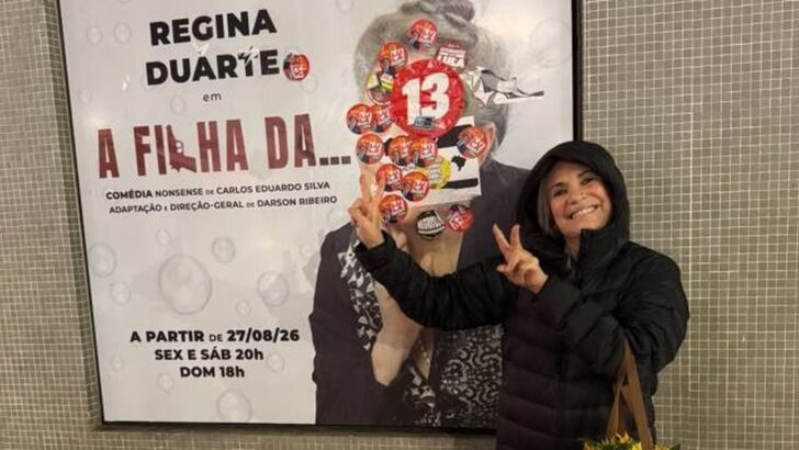 Regina Duarte faz o número 22 ao lado de cartaz de sua peça coberto por adesivos do PT
